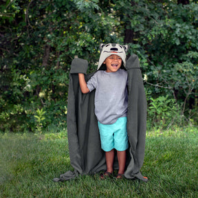 Child wearing a Aspen the wolf blanket in a grassy area with trees in the background